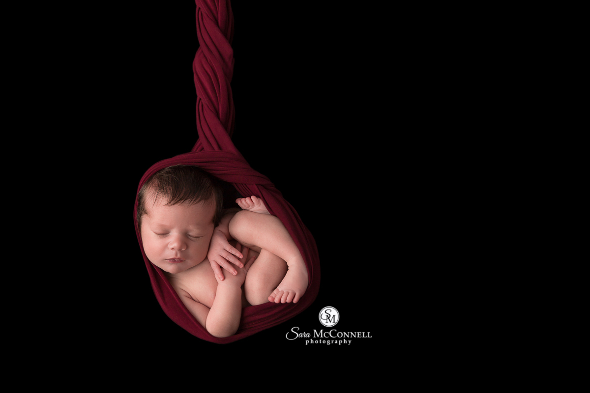 Newborn baby wrapped in a maroon cloth against a black background