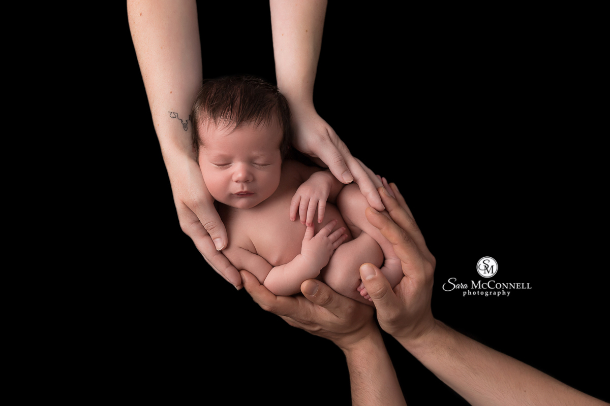 Parents hands holding newborn baby against a black backdrop