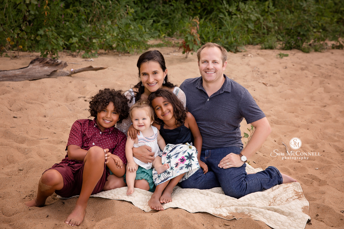 Family sitting on the beach for a photo by Sara McConnell Photography