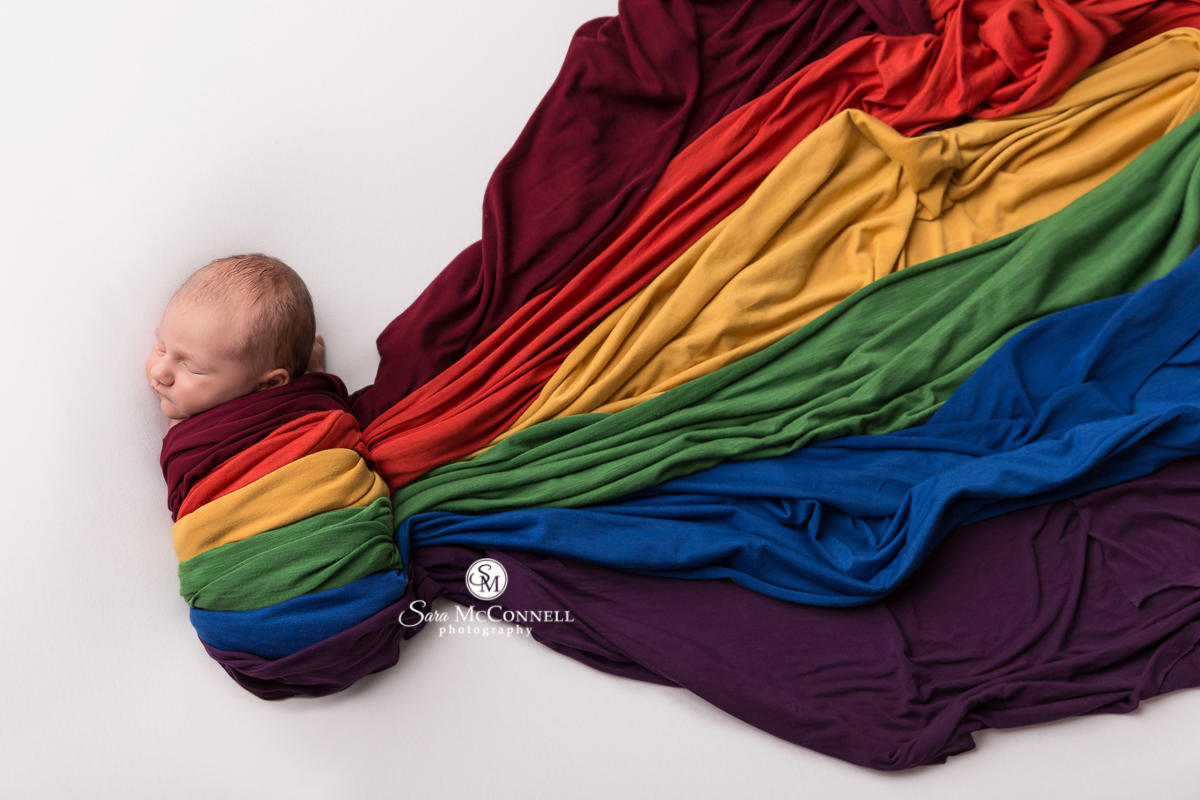 Newborn baby wrapped in a rainbow of colours in newborn photo session by Sara McConnell Photography
