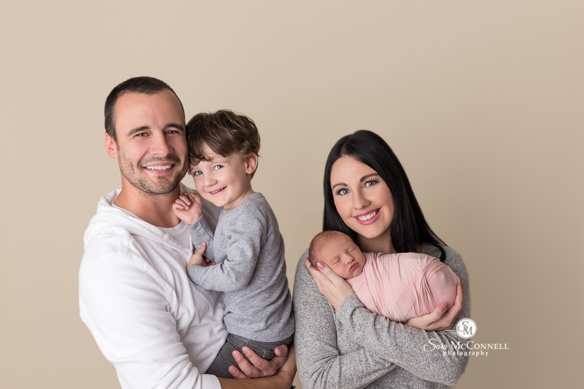 Father and son beside Mother holding her newborn baby during a newborn photo session with Sara McConnell Photography