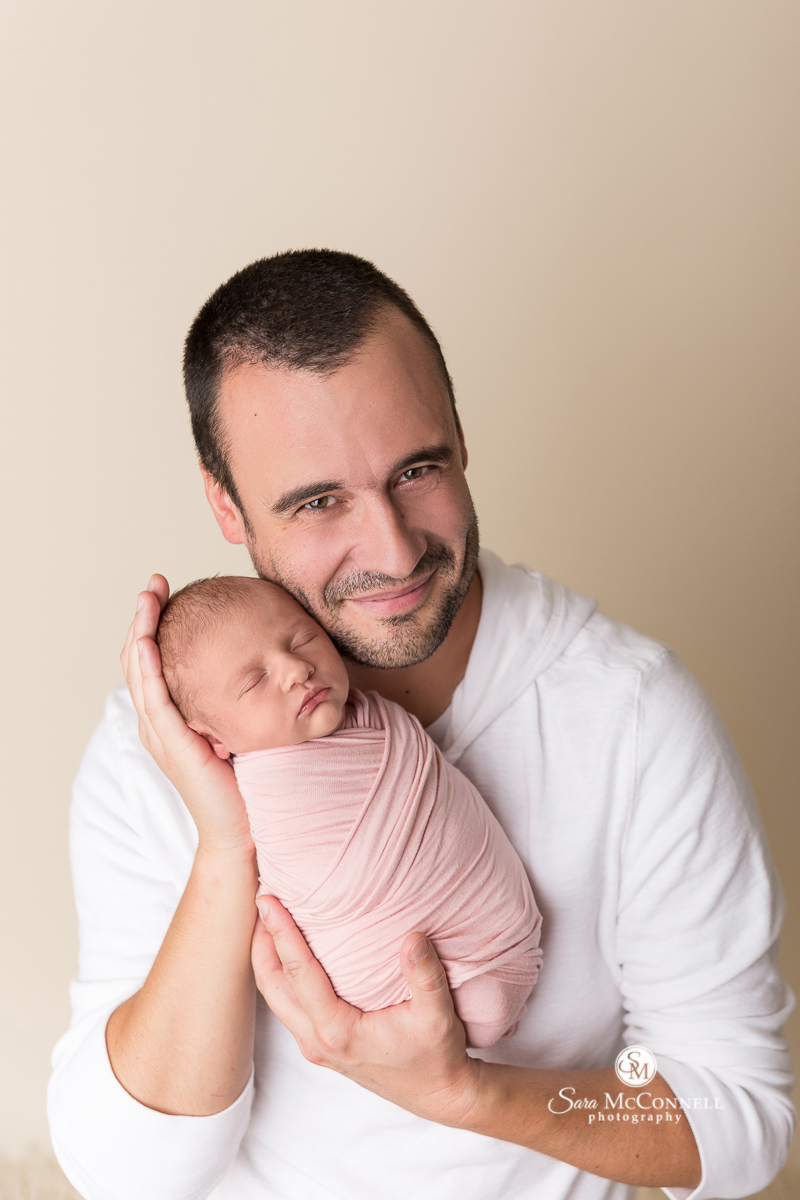 Father holding his newborn baby during a newborn photo session with Sara McConnell Photography
