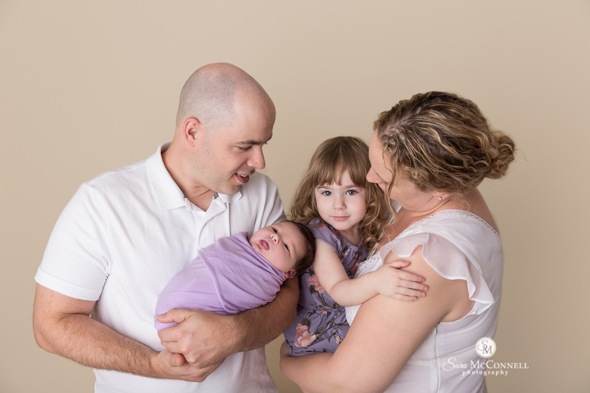 father holding newborn while mother holds small girl