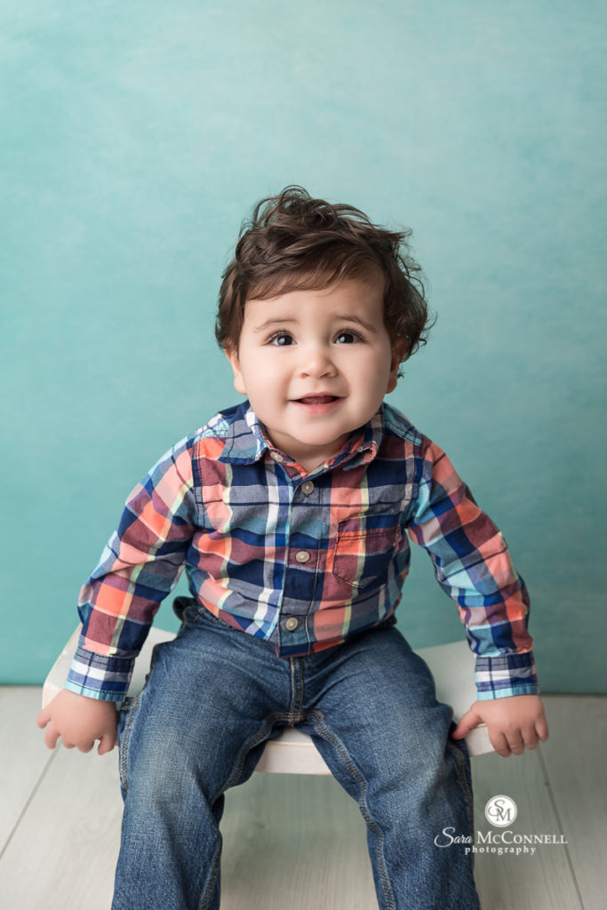 Boy wearing plaid shirt smiling in front of turquoise backdrop - photo by Sara McConnell Photography