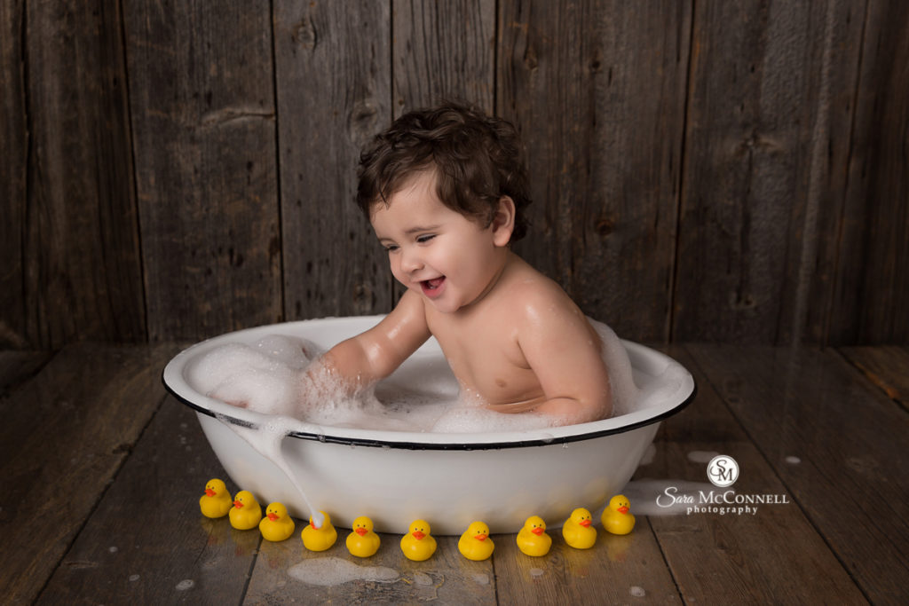 baby in bathtub surrounded by yellow rubber duckies