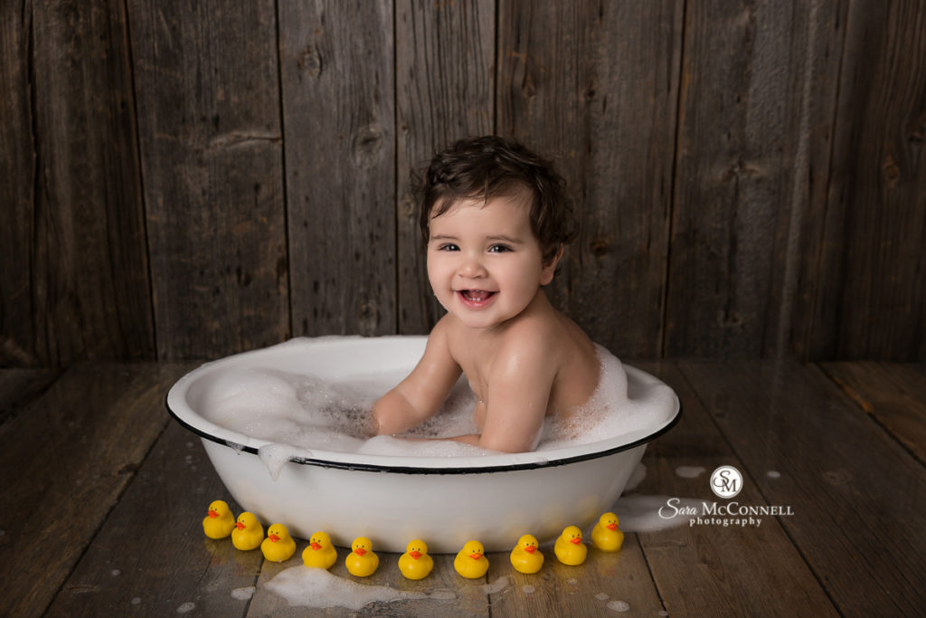 baby smiling while in bathtub surrounded by rubber ducks
