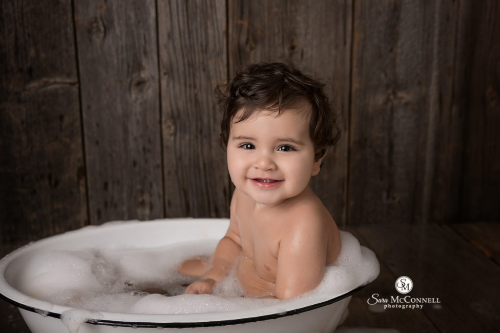smiling baby in  bathtub with bubbles on his face