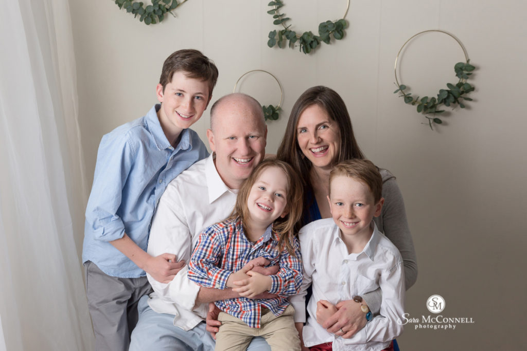 family of five smiling together in front of wall with wreaths