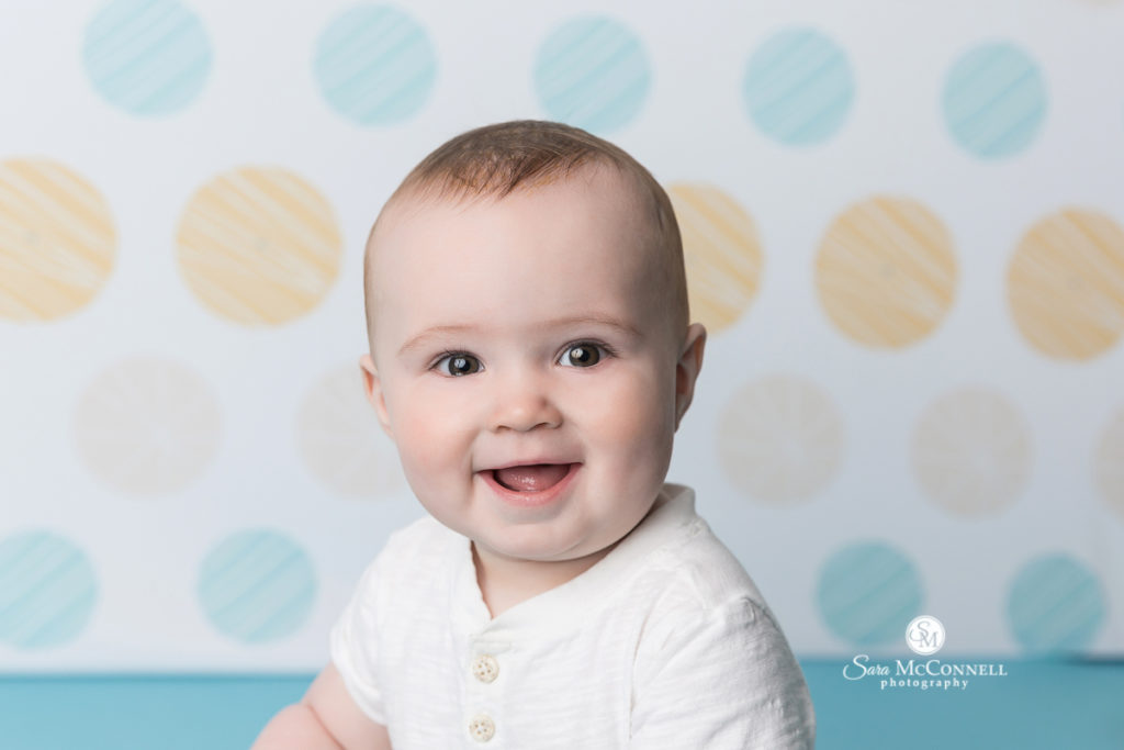 smiling baby in front of blue and yellow dots