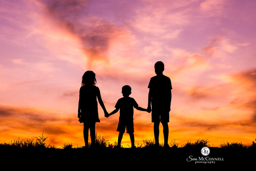 three children holding hands at sunset