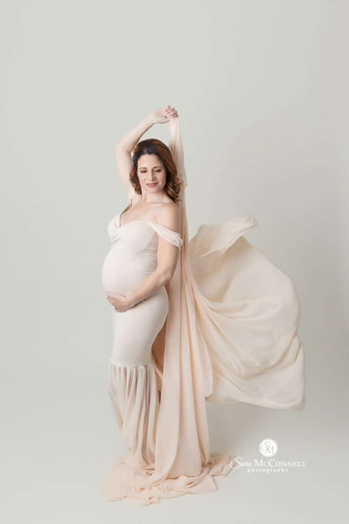 expectant mother in a cream coloured gown holding the extra fabric