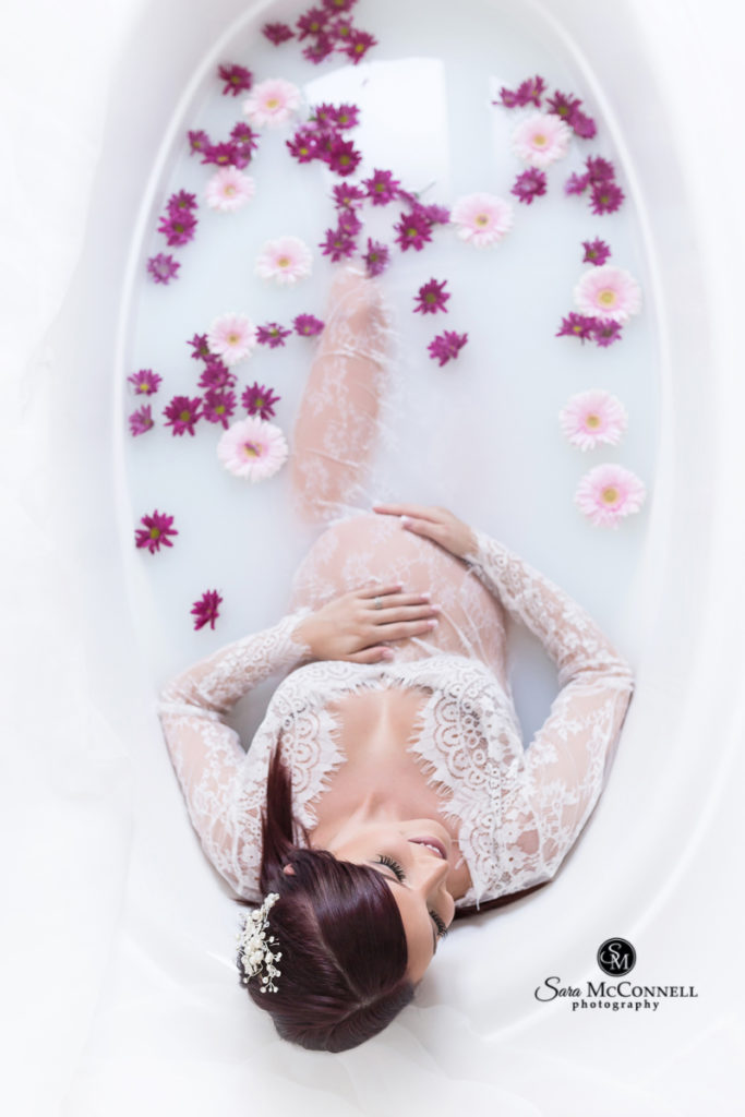 expectant woman in a lace gown in a milk bath with flowers
