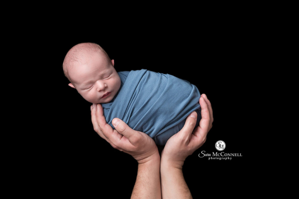 newborn baby wrapped in blue and held up by two hands