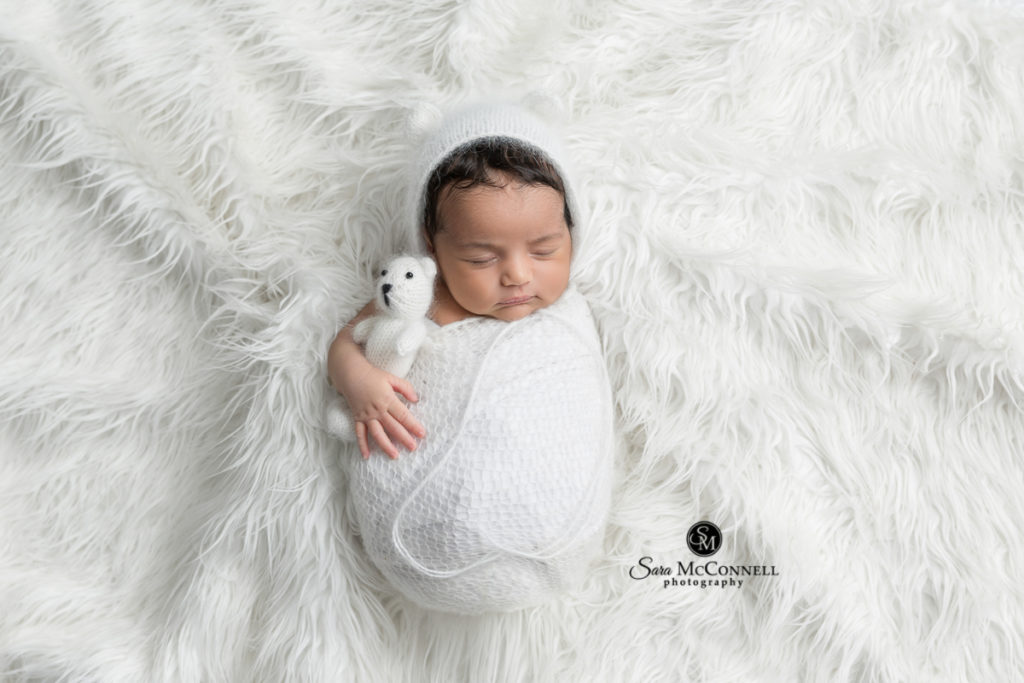 newborn baby wrapped in white on a fur rug