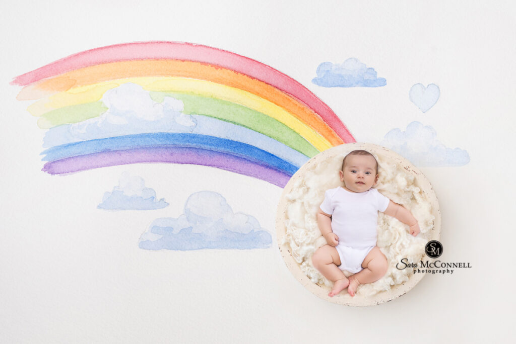 2 month old baby posed at the end of a rainbow
