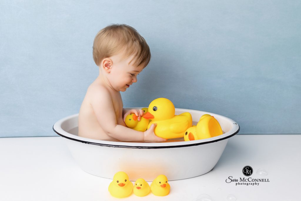 Baby sitting in a bathtub with rubber ducks in a blog post about baby bathtub photography sessions. Ottawa maternity photographer.