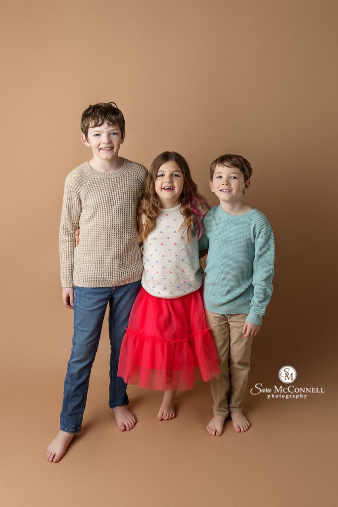 Photo of three children smiling at the camera in a blog post about Candid versus posed images. Ottawa maternity photographers.