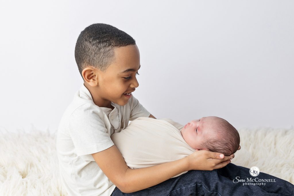 Big brother holding newborn sister in a blog post about soothing newborns during sessions. Maternity and newborn photography.