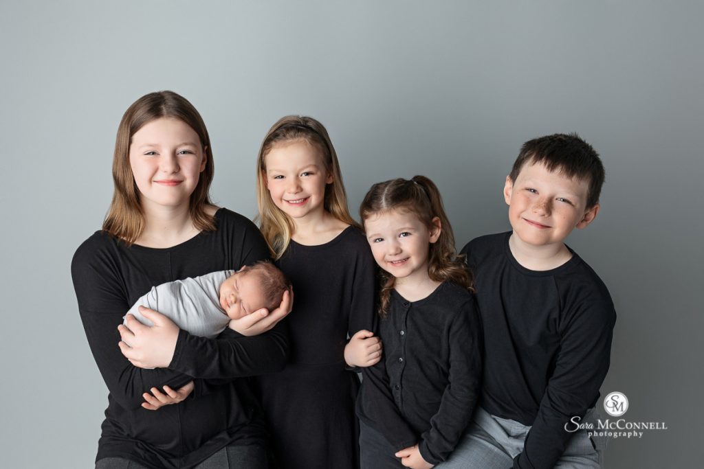 Photo of our children smiling at the camera while holding their newborn sibling in a blog post about editing client photos. Maternity photographers ottawa.