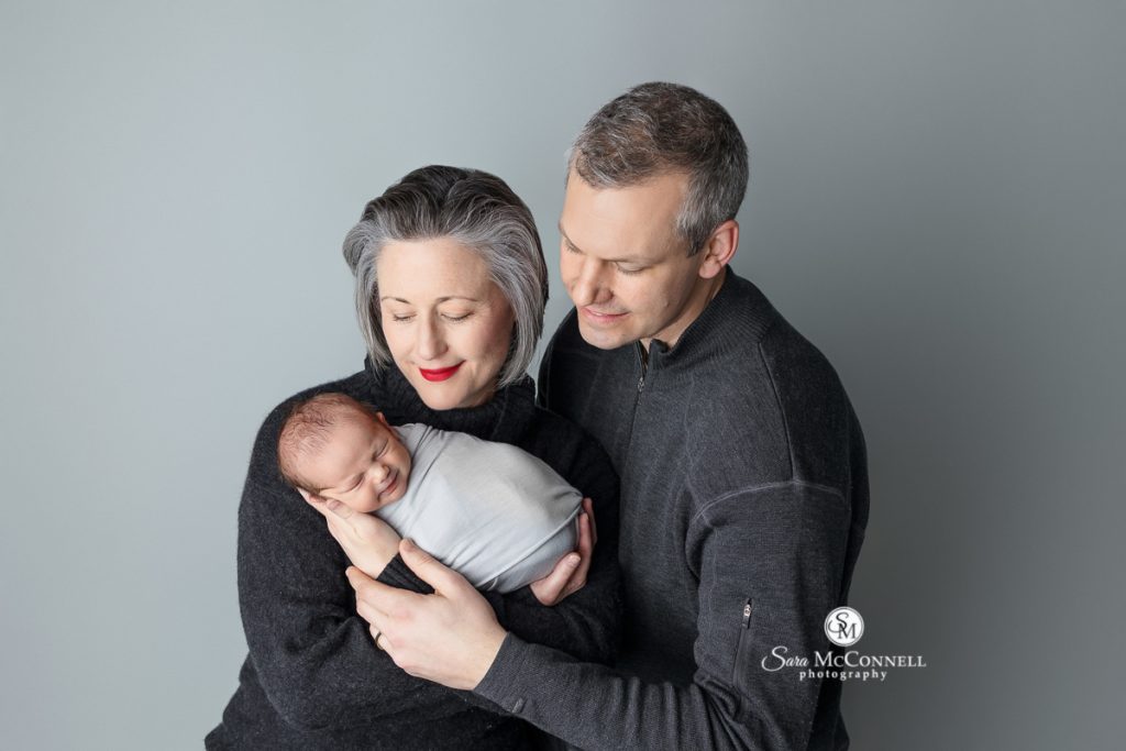 Photo of mom and dad smiling at their newborn while mom holds them in a blog post about editing client photos.  Maternity photographers ottawa.