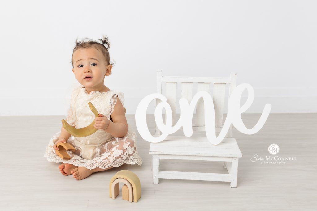 Photo of a one year girl playing with a wooden toy in a blog post about displaying first birthday photos. Maternity photographers ottawa.