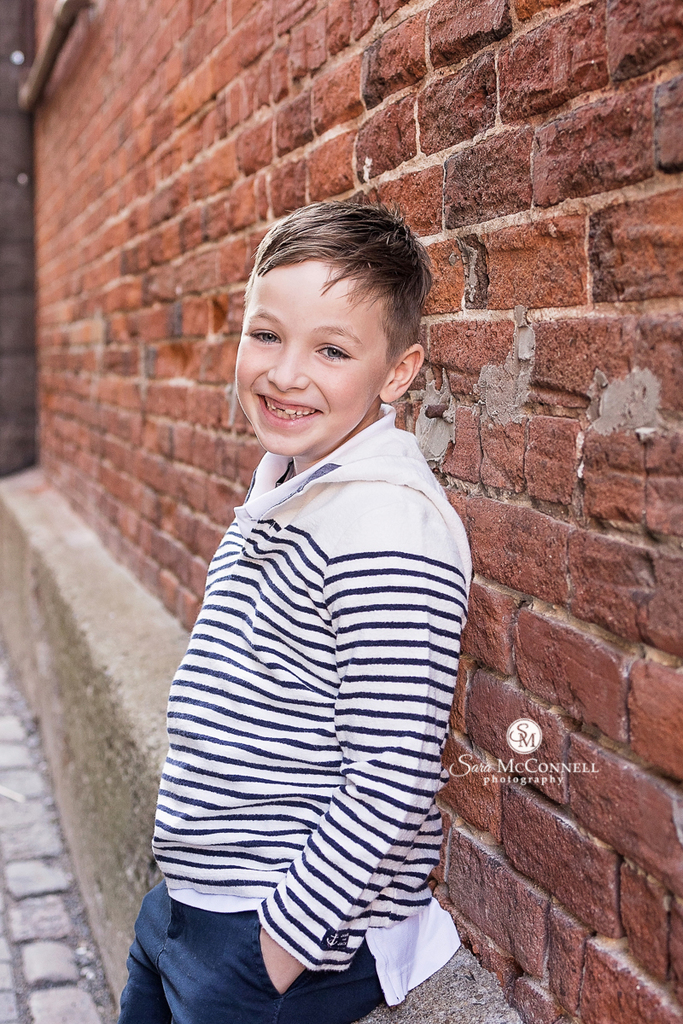 Photo of a boy leaning against a wall smiling in a blog post about Family Photos in Downtown Ottawa. Best newborn photographer ottawa.