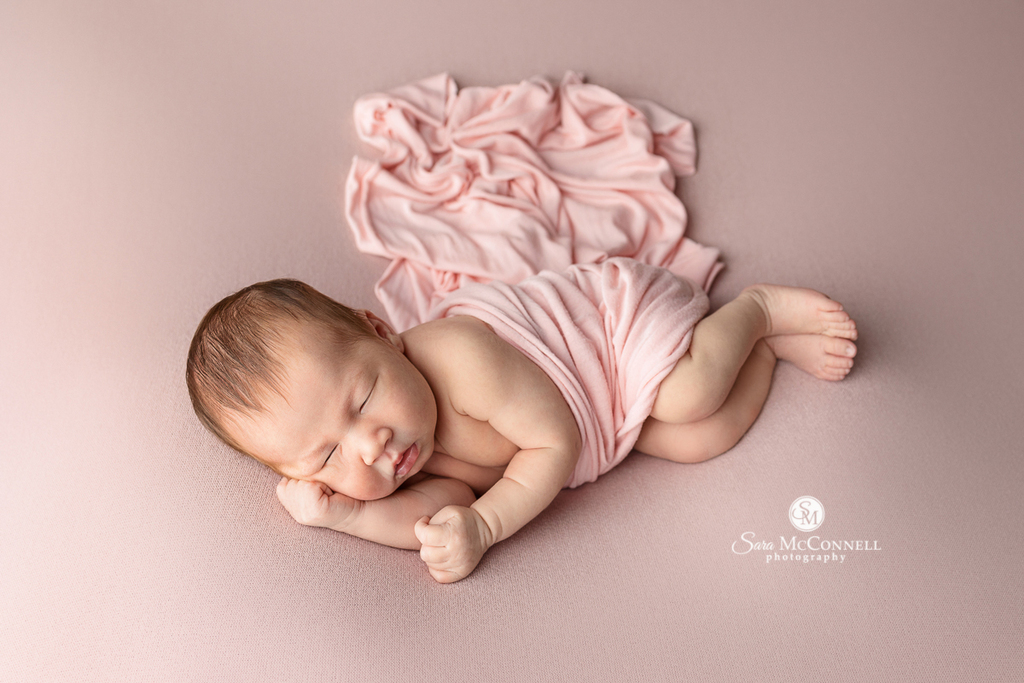 Photo of a newborn baby girl posed on pink fabric in a blog post called "What if my baby is awake?" Maternity photography near me.
