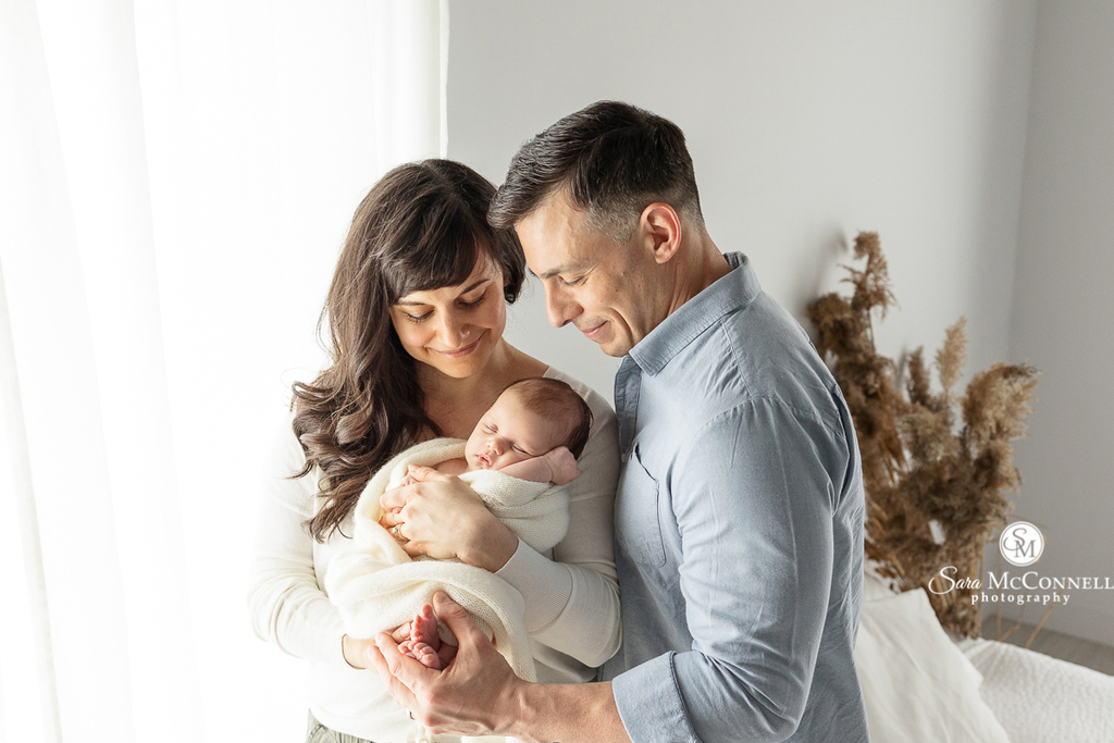 A photo of a mom and dad holding their newborn baby in blog post about Ottawa Lifestyle Newborn Photo Sessions. Maternity Ottawa.